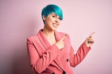 Young beautiful businesswoman with blue fashion hair wearing jacket over pink background smiling and looking at the camera pointing with two hands and fingers to the side.