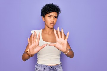 Young beautiful african american afro woman wearing casual t-shirt over purple background Moving away hands palms showing refusal and denial with afraid and disgusting expression. Stop and forbidden.