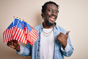 Poster - Young african american patriotic man holding united states flags over white background pointing and showing with thumb up to the side with happy face smiling