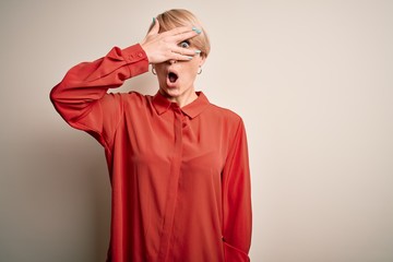 Poster - Young beautiful business blonde woman with short hair standing over isolated background peeking in shock covering face and eyes with hand, looking through fingers with embarrassed expression.