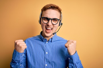 Wall Mural - Young handsome redhead call center agent man wearing glasses working using headset celebrating surprised and amazed for success with arms raised and open eyes. Winner concept.