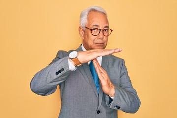 Middle age senior grey-haired handsome business man wearing glasses over yellow background Doing time out gesture with hands, frustrated and serious face