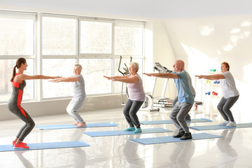 Young trainer exercising with elderly people during training in gym