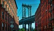Manhattan Bridge seen from a narrow alley enclosed by two brick buildings on a sunny day in Washington street in Dumbo, Brooklyn, NYC