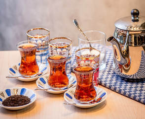 A group of traditional bardak glass of hot Turkish tea with metallic tea pot and loose tea