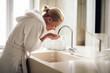 © JustLife - Beautiful woman enjoying in hotel. Young happy women in bathrobe wash her face.