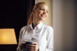 © JustLife - Beautiful woman drinking coffee in hotel room. Businesswoman working on lap top.