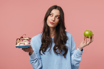 Poster - Image of thoughtful woman holding apple and sweet cake in her hands