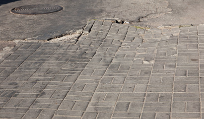 Canvas Print - Damaged road with potholes, caused by freeze-thaw cycles in winter. Bad road. Broken pavements sidewalks on sidewalk. pavement with paving slabs with defects and cracks coming in perspective