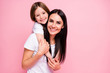 © deagreez - Photo of pretty young mommy hold arms hugging little daughter good mood lovely sincere cardiac feelings piggyback wear casual t-shirts jeans isolated pastel pink color background