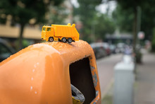 Close-up Of Yellow Toy Truck On Garbage Bin