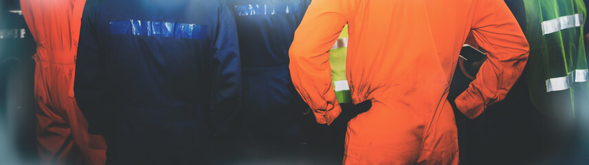 Rear view group of industrial technicians wear safety work clothes to be effective.