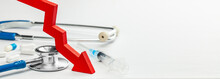Red Down Arrow And Medical Devices. White Background With Stethoscope, Syringe And Pills. Copy Space For Text
