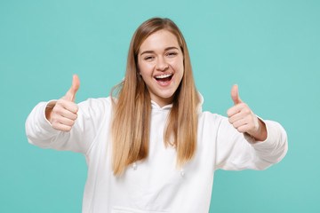 Cheerful young woman girl in casual white hoodie posing isolated on blue turquoise wall background studio portrait. People sincere emotions lifestyle concept. Mock up copy space. Showing thumbs up.
