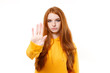 © ViDi Studio - Serious young redhead woman girl in casual yellow hoodie posing isolated on white background studio portrait. People emotions lifestyle concept. Mock up copy space. Showing stop gesture with palm.