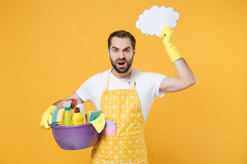 Wall Mural - Confused man househusband in apron rubber gloves hold basin detergent bottles washing cleansers doing housework isolated on yellow background. Housekeeping concept. Hold empty Say cloud speech bubble.