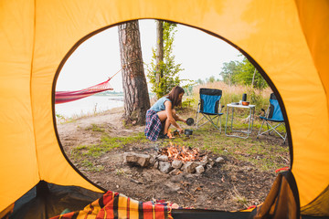 Wall Mural - view from camping tent woman cooking on burner near bonfire