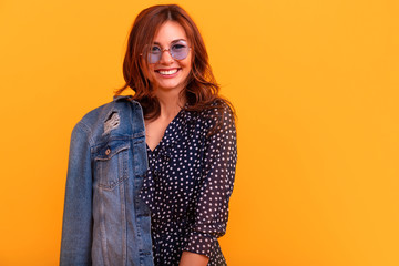 Winsome girl in romantic  pretty smiling woman on yellow background. Slim curly female model in polka dot dress and jeans coat looking to camera with happy positive face expression.