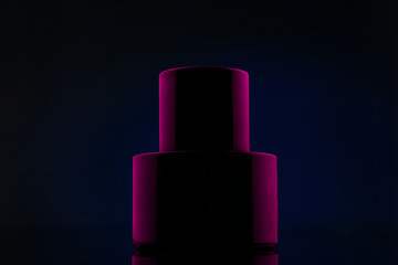 Wall Mural - Bottle of black perfume in pink light on a blue background. Cosmetic perfume black