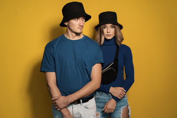 Portrait young pretty man and woman in blue t-shirts and black caps posing on yellow background