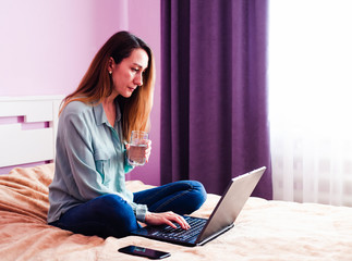 Attractive young woman holds glass of water working with laptop. Home office.