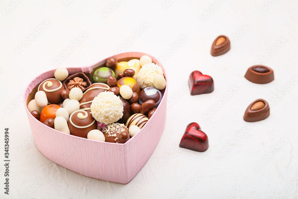 Heart-shaped box with delicious candies on white background