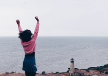 Woman With Arms Raised Standing Against Sea