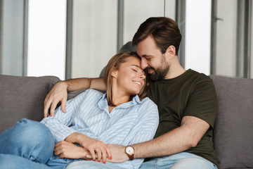 Wall Mural - Photo of cheerful couple smiling and hugging while sitting on sofa