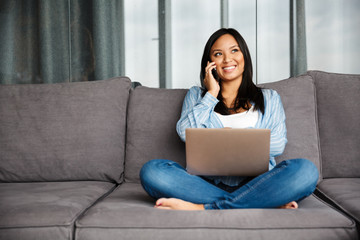 Wall Mural - Photo of smiling pregnant woman talking on cellphone and using laptop