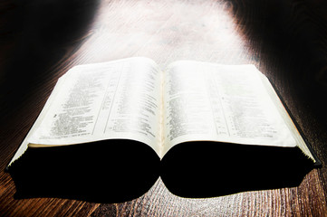 open book on a wooden background. holy bible on the table. the light through the window falls on the pages