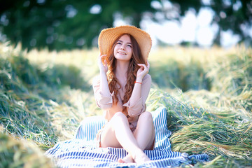 girl sitting in a field with a straw hat / summer vacation, rest young adult happy woman