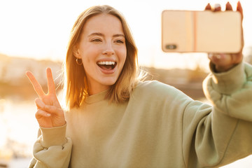 Poster - Portrait of woman gesturing peace sign and taking selfie on cellphone