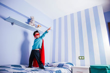 Little Boy Playing Super Hero, Standing On His Bed