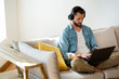© Westend61 - Young man sitting on couch at home with headphones and laptop