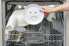 Poorly Washed Dishes In The Dishwasher. Integrated Dishwasher With White Plates Front Vew And Sad Emotion On Plate. Broken Dishwasher Machine Concept