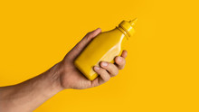 Unrecognizable Guy Holding Bottle Of Mustard On Orange Background, Space For Your Design. Panorama