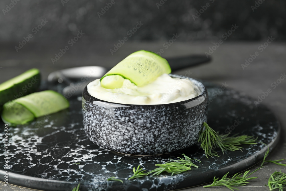 Delicious yogurt sauce with cucumber in bowl on dark background