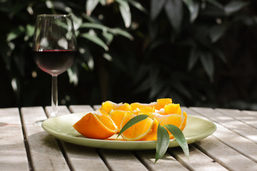 Red wine served outside in garden on white table with fresh orange in sun lights close up