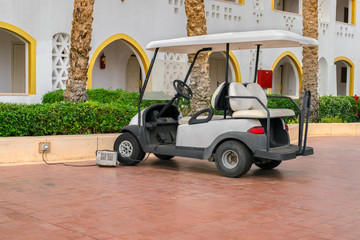 A white Golf cart is parked near the hotel complex. The electric car is charged in the Parking lot of the resort city. A car standing alone.