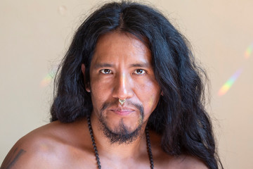 Portrait of young hispanic man with long hair wearing a metal septum piercing at his nose