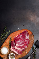 Wall Mural - Raw beef steaks on a cutting board, herbs and spices on a black concrete background top view, copy space. Cooking meat on a dark background, free space for text.