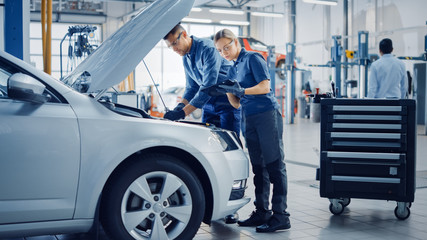 Wall Mural - Two Mechanics in a Service are Inspecting a Car After They Got the Diagnostics Results. Female Specialist is Comparing the Data on a Tablet Computer. Repairman is Using a Ratchet to Repair the Faults.