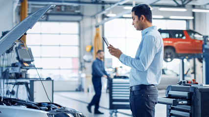 Wall Mural - Car Service Manager Uses a Tablet Computer with an Augmented Reality Diagnostics Software. Specialist Inspecting the Car in Order to Find Broken Components Inside the Engine Bay.