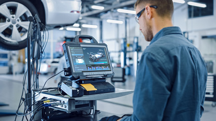 Wall Mural - Car Service Manager or Mechanic is Running an Interactive Diagnostics Software on an Advanced Computer. Specialist Inspecting the Vehicle in Order to Find Broken Components and Errors in Data Logs.