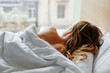 young Woman relaxes sleeping a beautiful and comfortable bed in front of the panoramic window with the head on the pillow to enjoy the sleep. Bare shoulder, rear view.