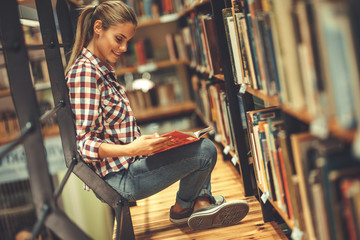 Wall Mural - Young female student read and learns by the book shelf at the library.Reading a book.	
