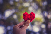Cropped Hand Holding Red Knitted Heart Shape Wool Decoration In Park