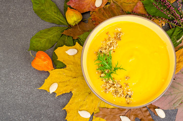 Wall Mural - Hot pumpkin soup on background of dried autumn leaves.