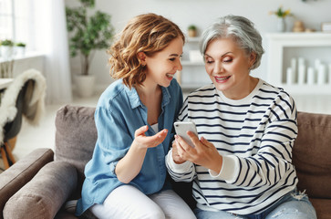 Cheerful mother and daughter using smartphone on sofa.