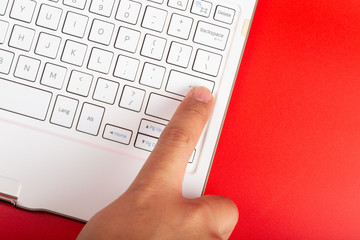 Man hand press ENTER button on white keyboard isolated on red background.